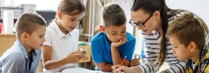 Lehrerin korrigiert umring von Kinder in einem Schreibheft.