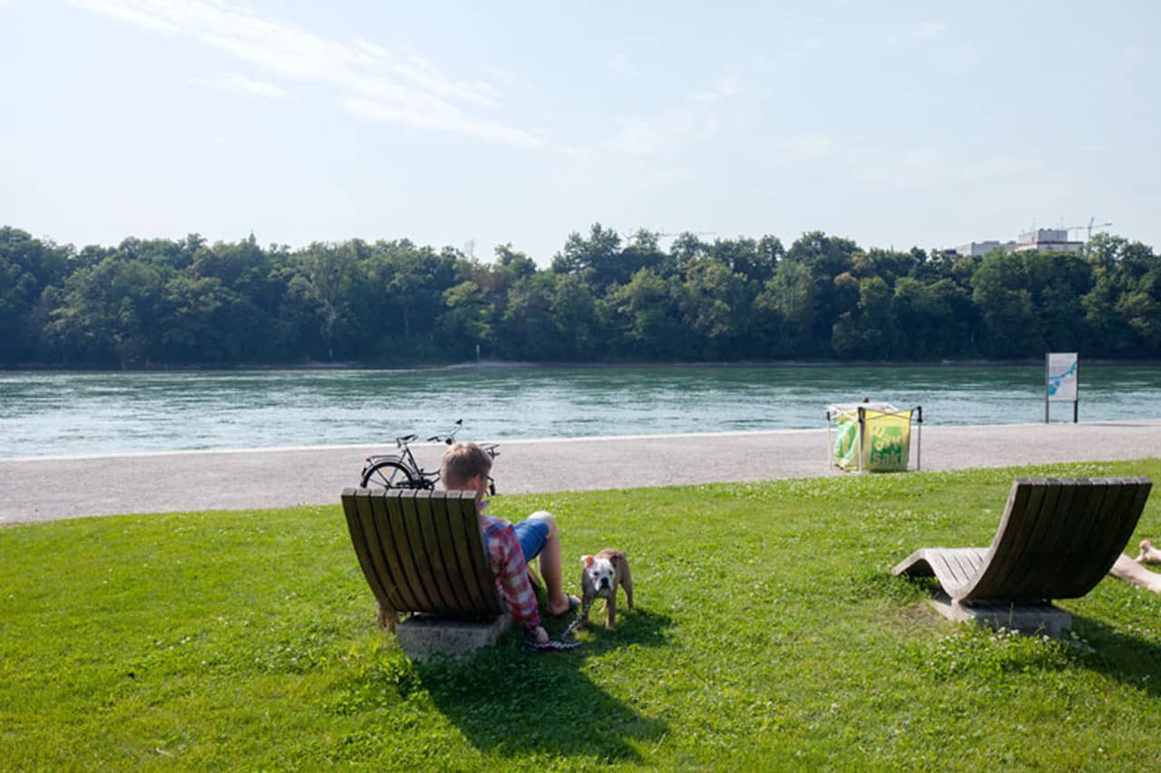 Ein Mann mit Hund sitze auf einer Holzliege mit Blick Richtung Fluss