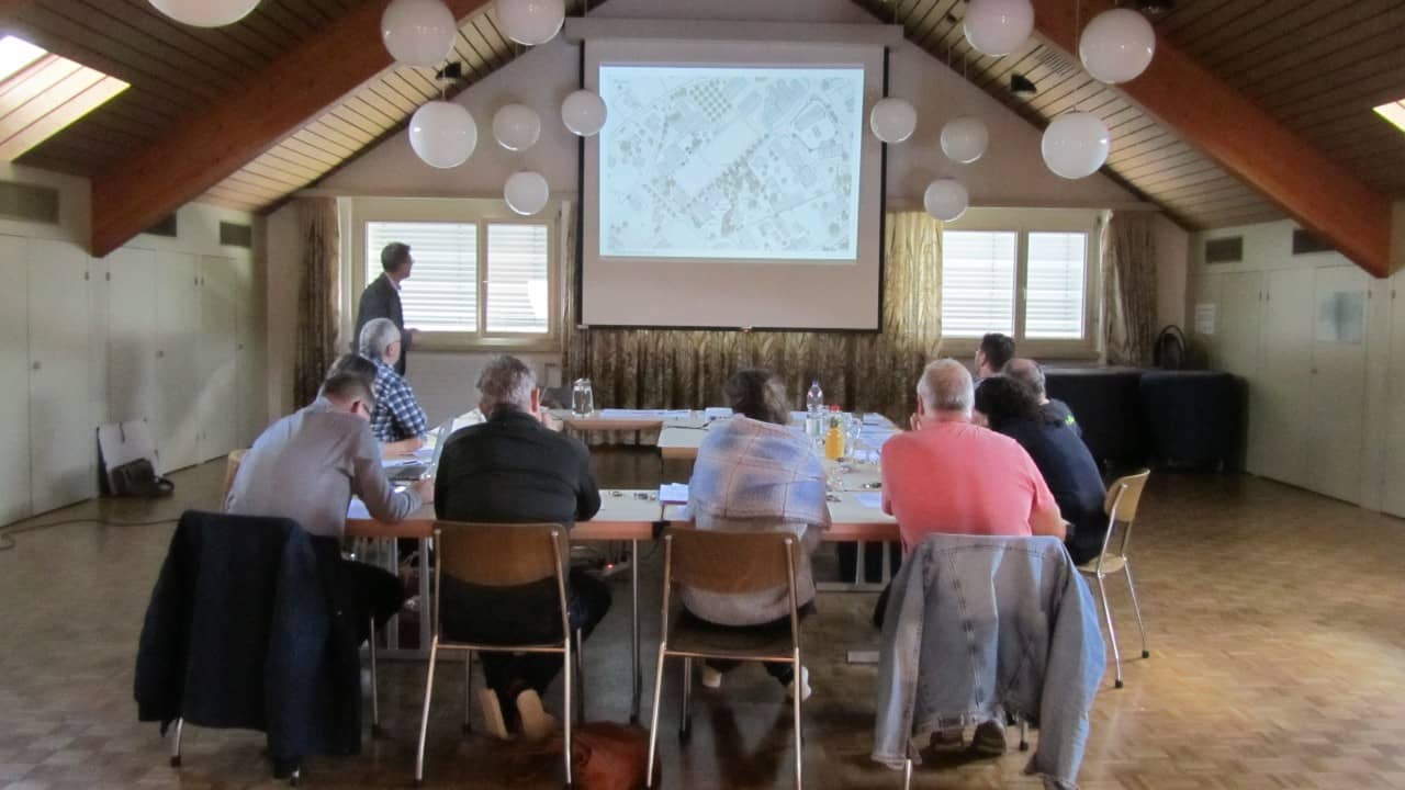 Das Begleitgremium folgt dem Vortrag eines der Landschaftsarchitekten. Es wird eine Präsentation auf eine Leinwand projiziert.